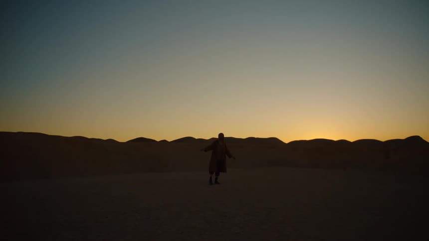 Man standing in desert near rocky hills falls to his knees under a red sky