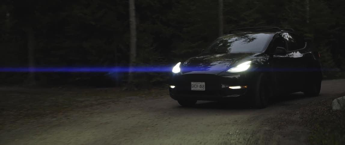 An electric vehicle slowly navigates around a bend in a road lined with trees
