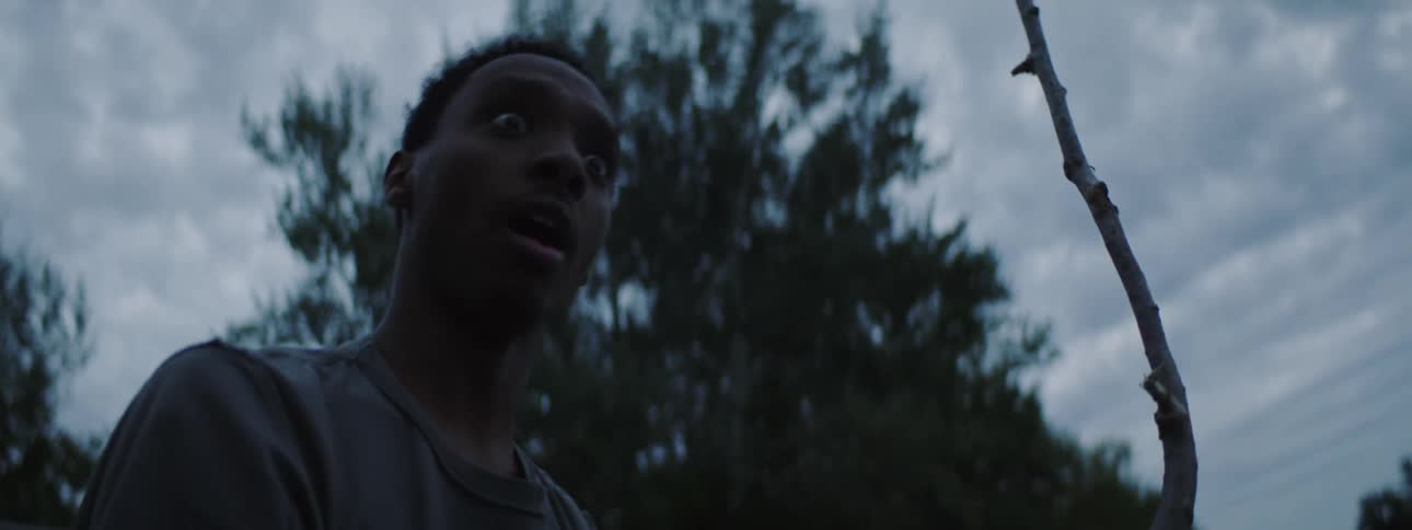 A young man with a branch in his hand slamming it on the ground and looking surprised at the person in front of him