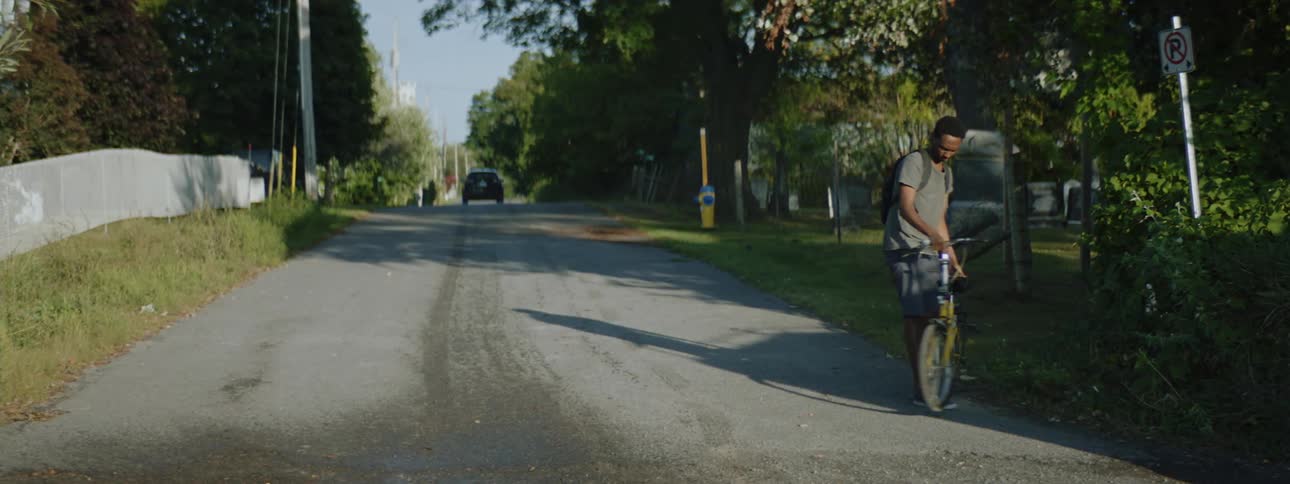 A teenager gets on his bike as a car drives past