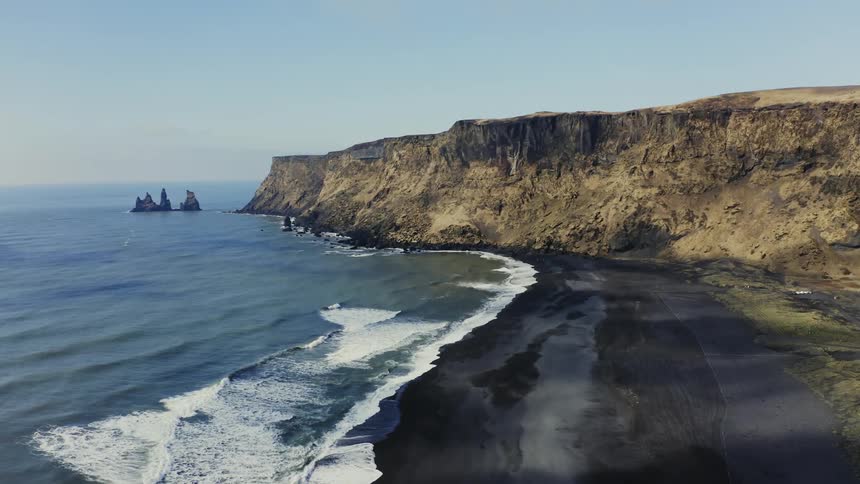 Aerial view of black sand beach and cliffs next to ocean