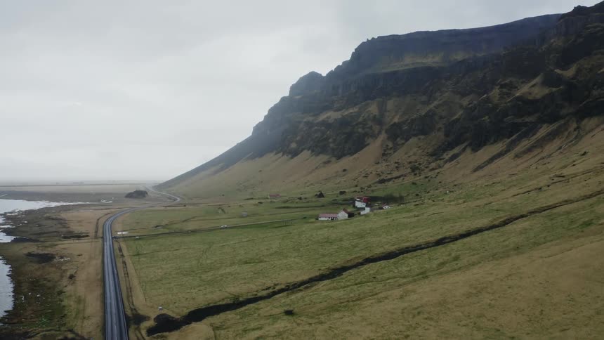 A road follows the coastline next to a cliff covered in grass