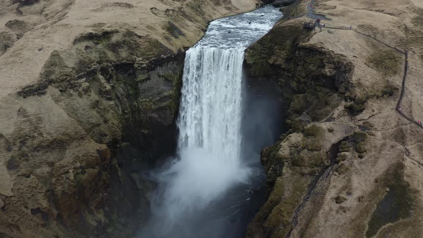 Waterfalls flow over the side of a mountain cliff as birds fly over the water