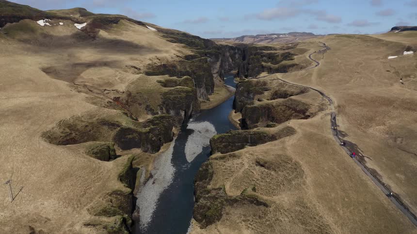A drone view of a river running through a canyon at a national park where a walking trail follows it along the ridge