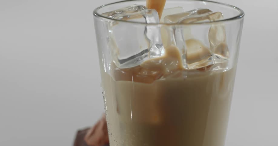 A glass filled with ice being filled with a creamy vanilla liquid