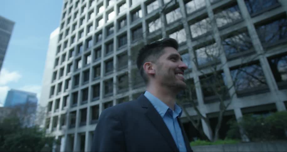 A smiling man walks through a city on a sunny day