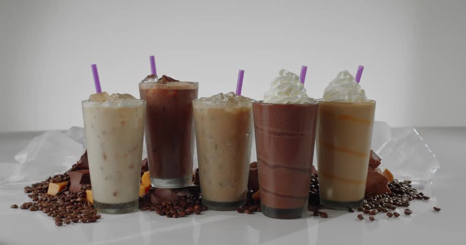 Iced coffee drinks and milkshakes on a countertop with coffee beans