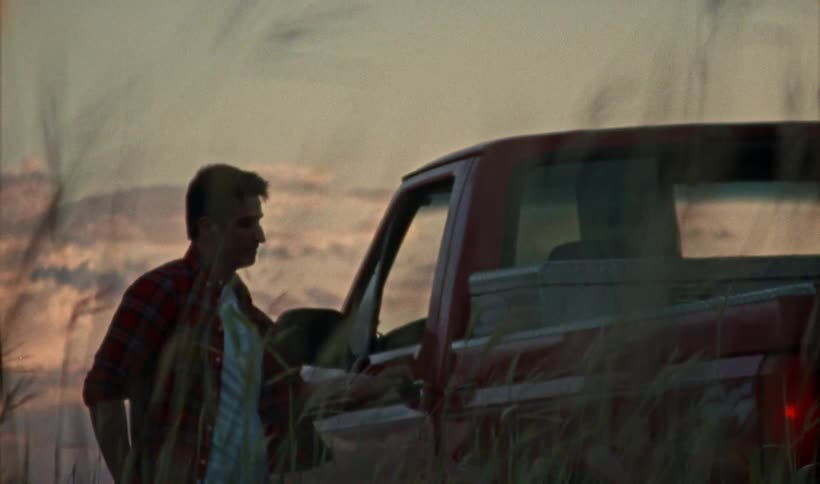 A man is standing in front of his pickup truck while watching the sun set before getting in his truck to leave
