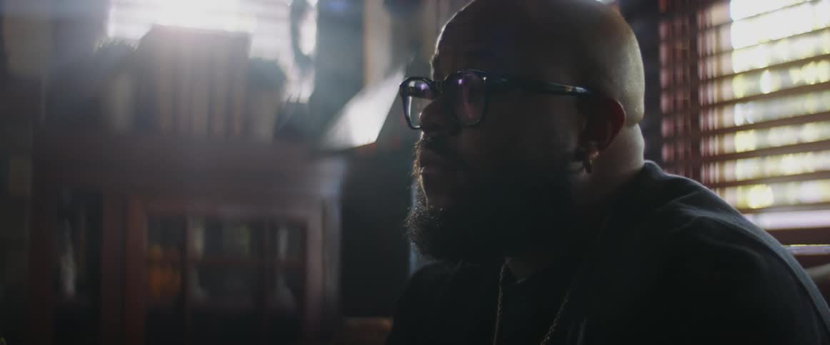 A bald bearded man sitting on a living room sofa