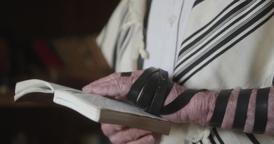 Close up of the hand of a jewish man wearing the straps of a terillin around his arm while reading scriptures