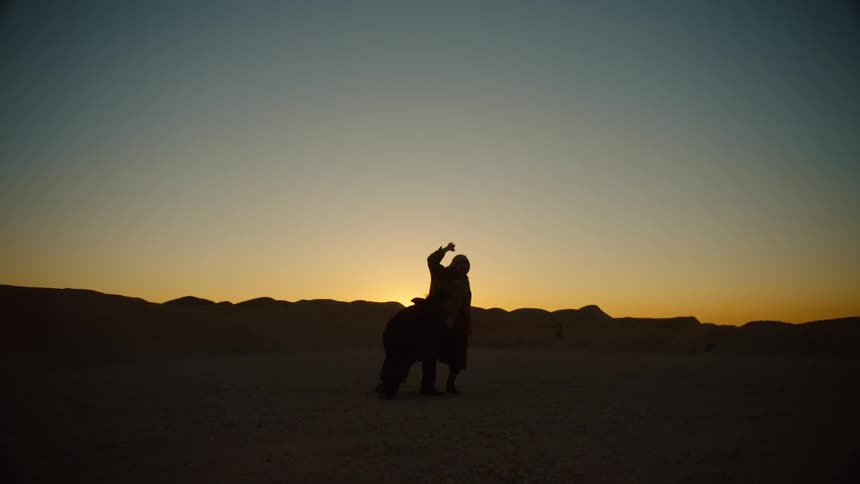 Two dancers dance on sands against mountains and a red horizon
