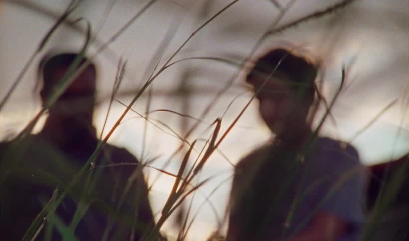 Father with glasses a goatee and a shirt talks with son in t shirt in the windy field at sunset