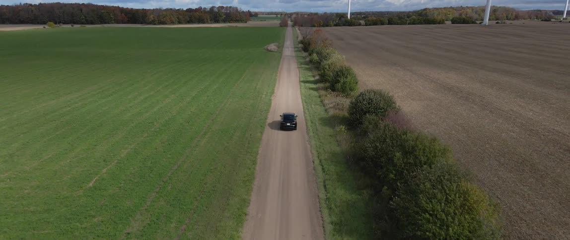 Aerial view of black electric car driving along country road near the green field