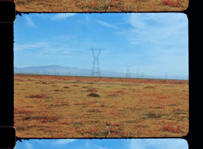 Electricity transmission towers on a field under a blue sky caught on vintage film