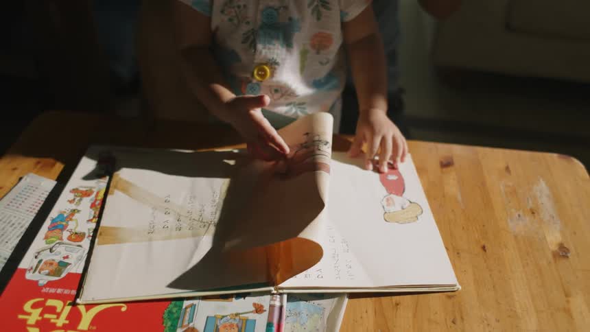 A small child flipping through book pages on a wooden table in front of them
