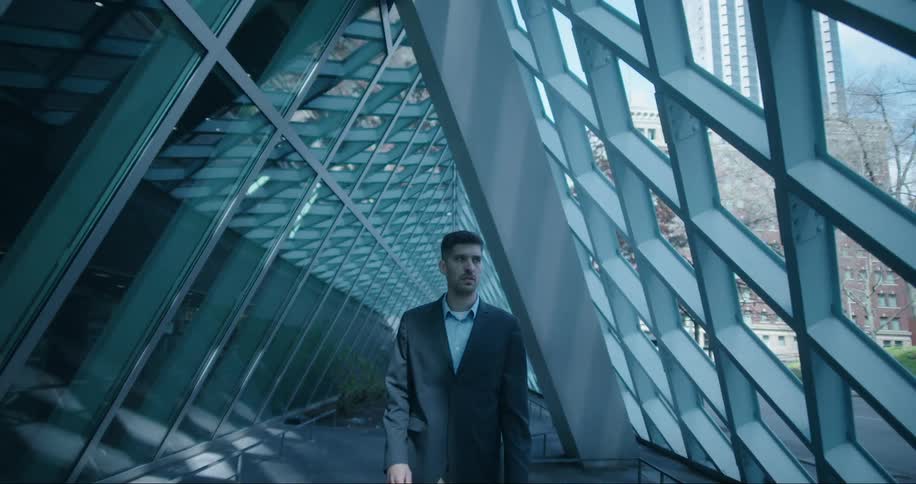 A man walks through a tunnel of modern architecture filled with windows showing downtown buildings