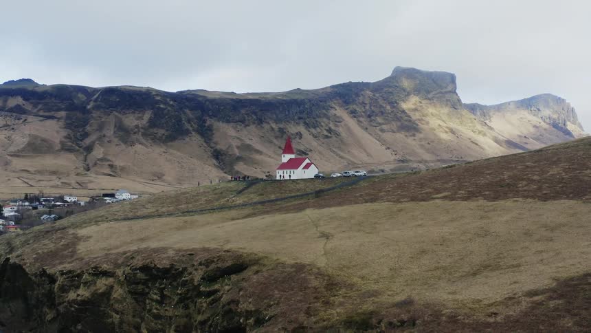 Aerial view of a small white church with red roof on a hill near a small town in the mountains