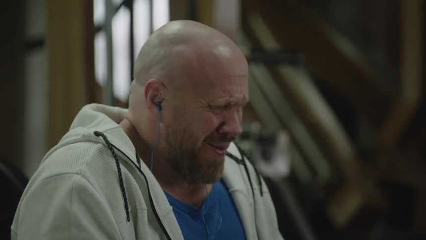 A man sitting on a workout bench taking deep breaths then getting upset and rocking back and forth