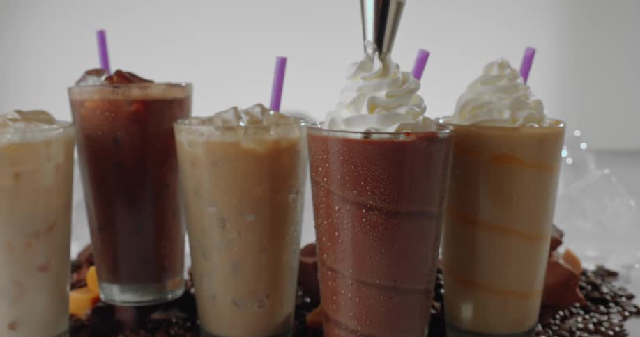 A close up of whipped cream being spread on a drink then a wide shot of multiple sweet drinks on a table