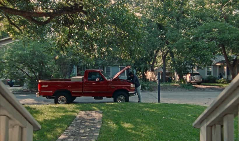 Person working on a truck with hood up in the front yard