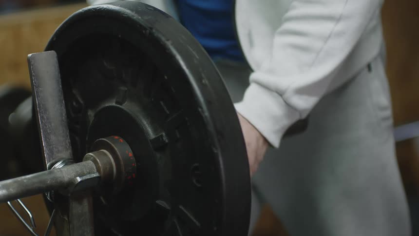 A person attaches weights on a barbell and secures them in place with a clamp