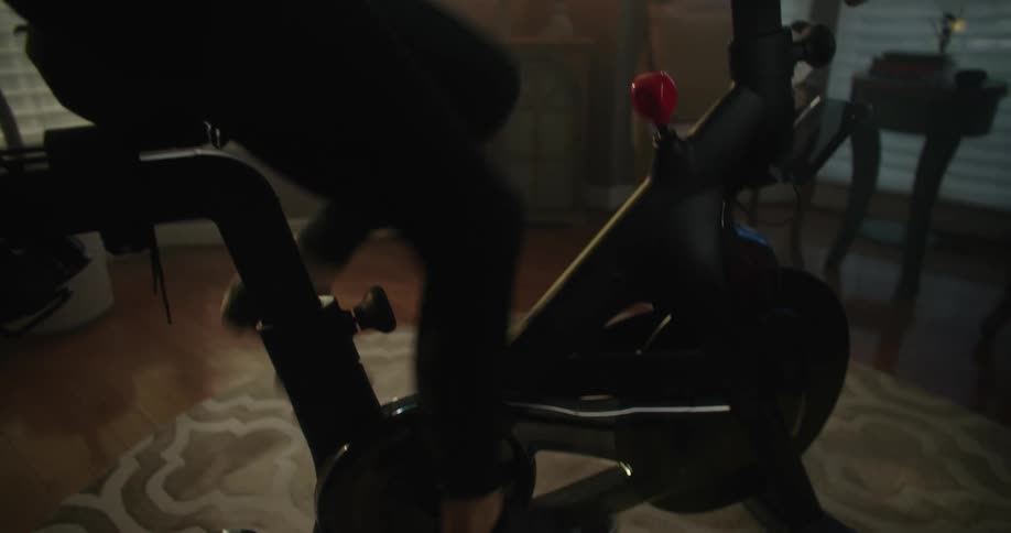 A woman pedals vigorously on a stationary bicycle in a house
