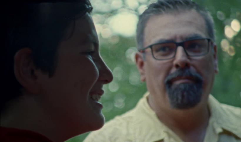 A father and son talking outdoors near trees as they smile and laugh