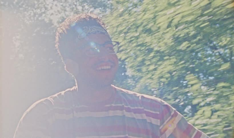 A man is smiling while traveling down a tree lined road on a sunny day
