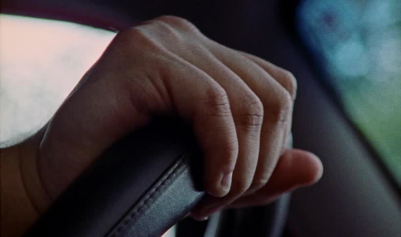 A hand closes its grip on a leather covered steering wheel