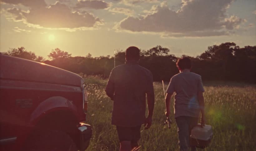 A father and son walk together through a meadow on their way to go fishing