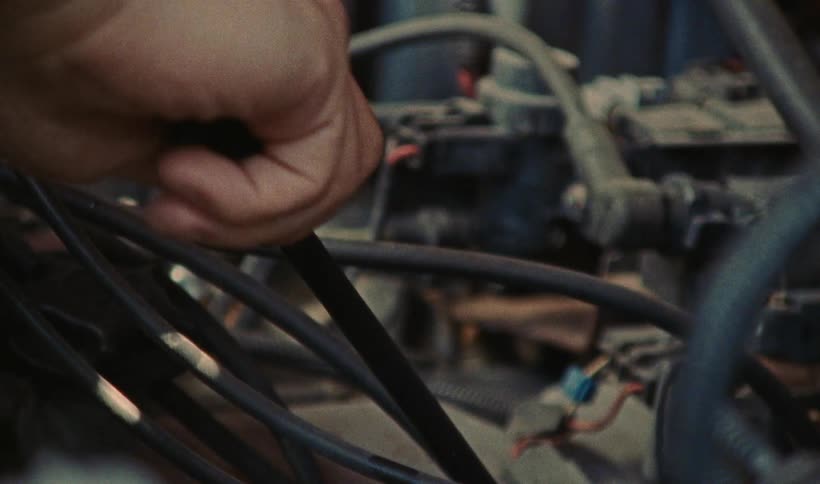 A close up of a vehicle motor and wires while a person puts a dipstick into its holder