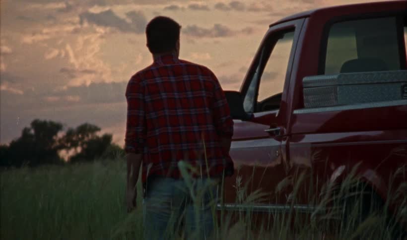 A man gets out of his pickup truck and walks in the grass