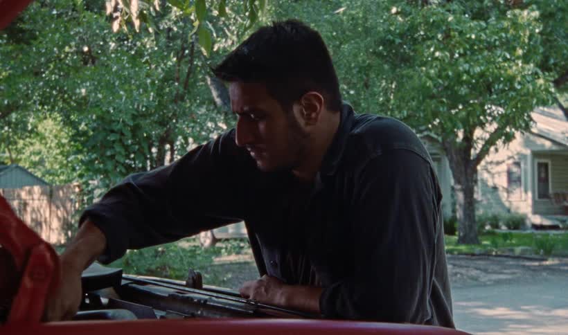 A man uses a wrench to work on a car engine in a yard