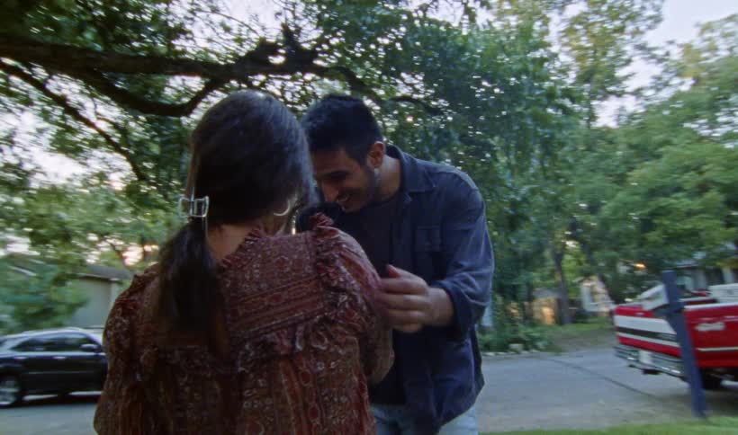 Man fixing a pickup truck in the garage at home greets her wife and daughter with a hug in the front yard