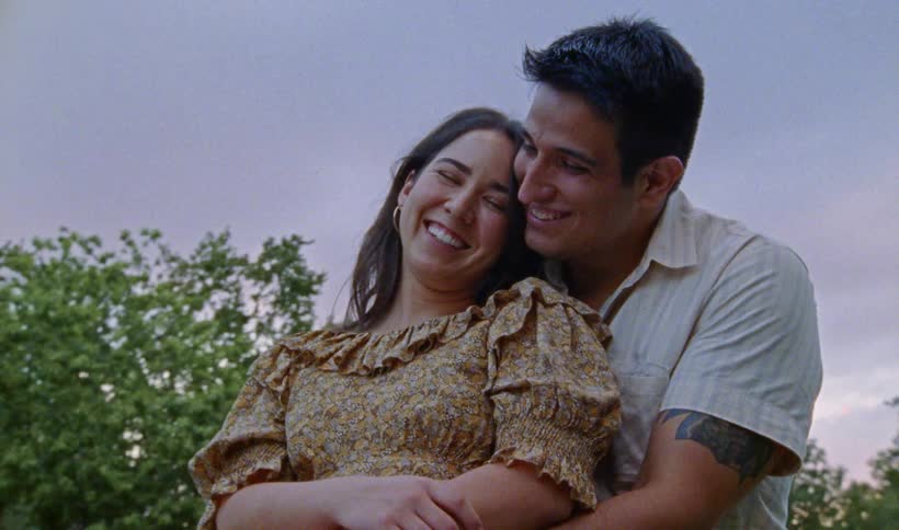 A man and woman cuddle while talking and laughing together during sunset