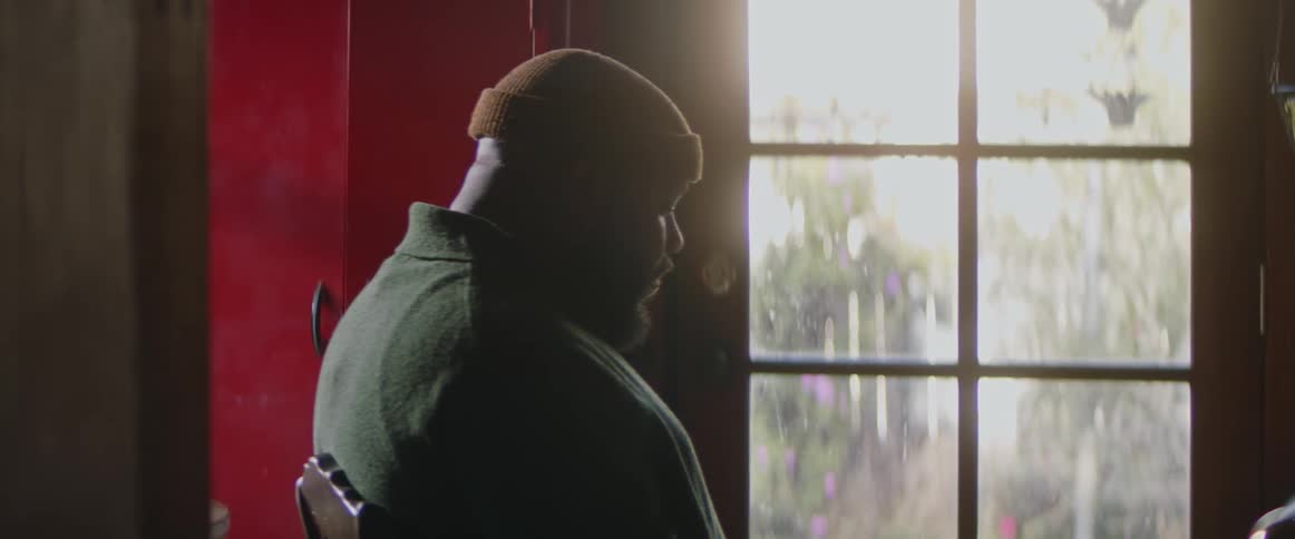 A black man wearing a cap is sitting in a chair looking contemplative