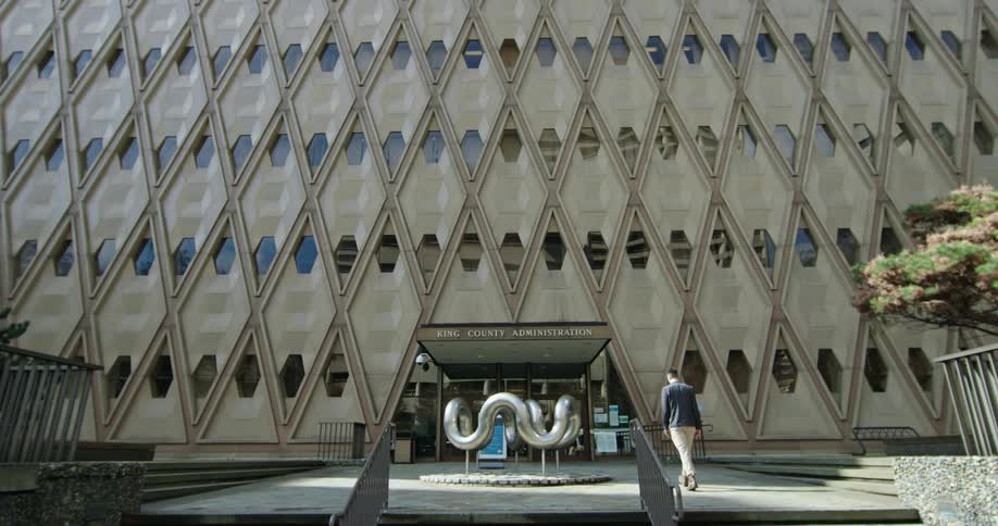 Man climbs steps and moves past abstract sculpture near door to government building with hexagonal windows