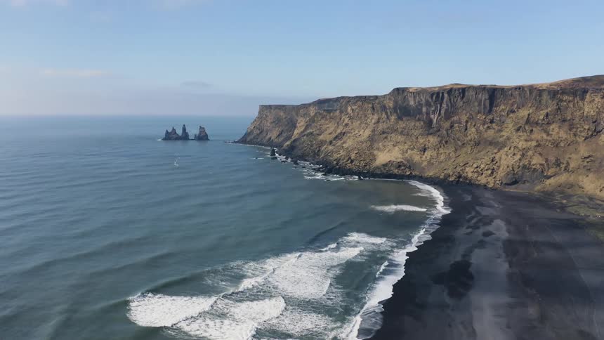 Aerial of waves crashing on shoreline of a black sand beach