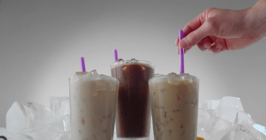 Man adds straw to one of the icy drinks surrounded by ice chunks and coffee beans