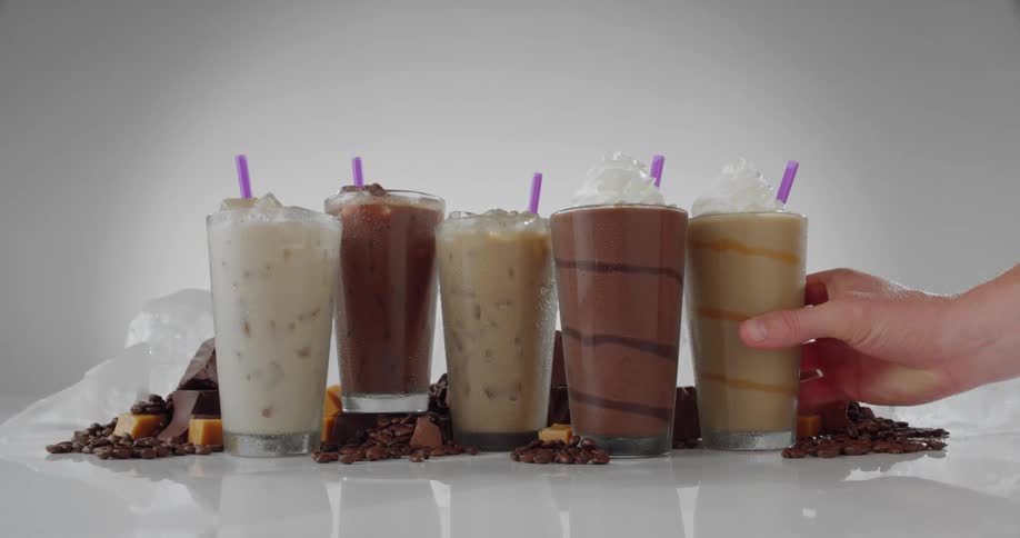 Person adds another frozen coffee drink to other drinks posed among coffee beans and chunks of chocolate and caramel