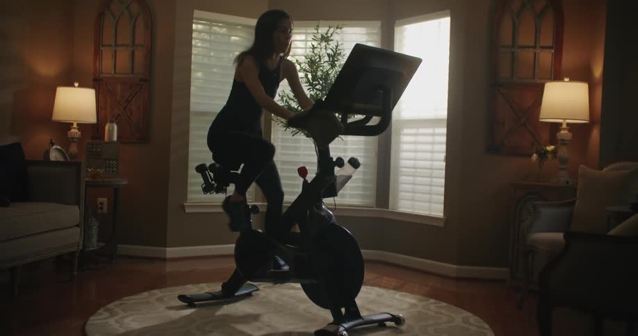 A woman exercising on her home bike in her living room as light shines through the window