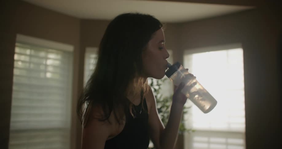 A woman is riding an exercise bike and she takes a drink from her water bottle as she pedals