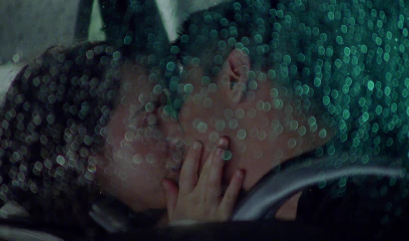 Couple kisses in vehicle at night as the headlights of passing vehicle lights them