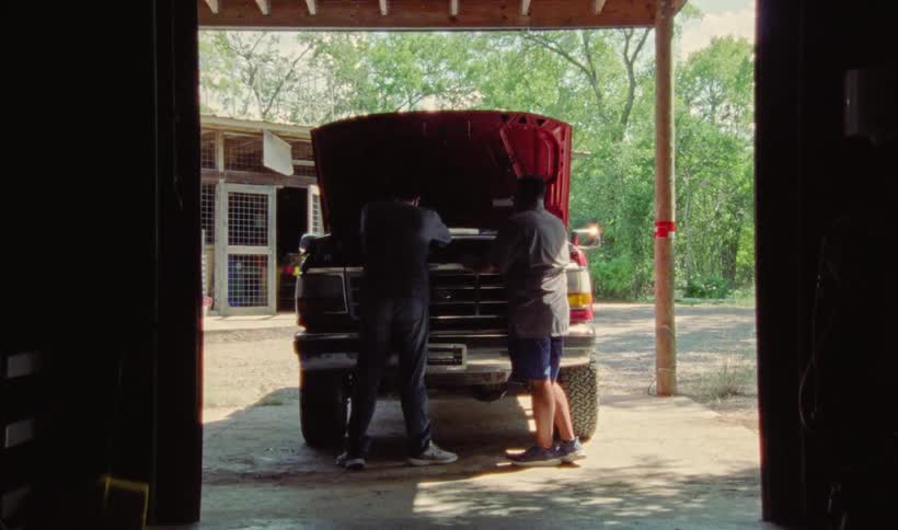 Two men working under the hood of a pickup truck in a carport