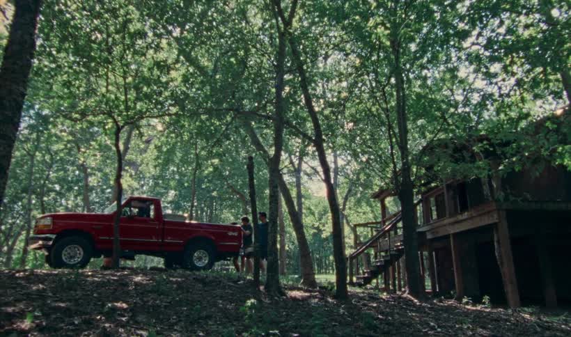 Three men leave house set on stilts and get into red pickup truck in wooded area