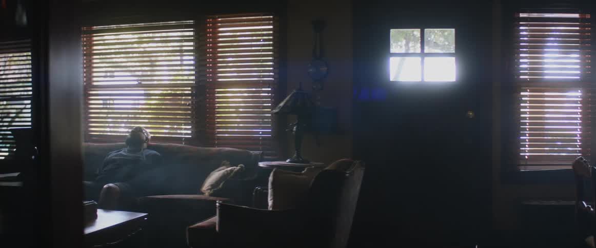 A man sitting on his couch in his living room as sunlight shines through the windows