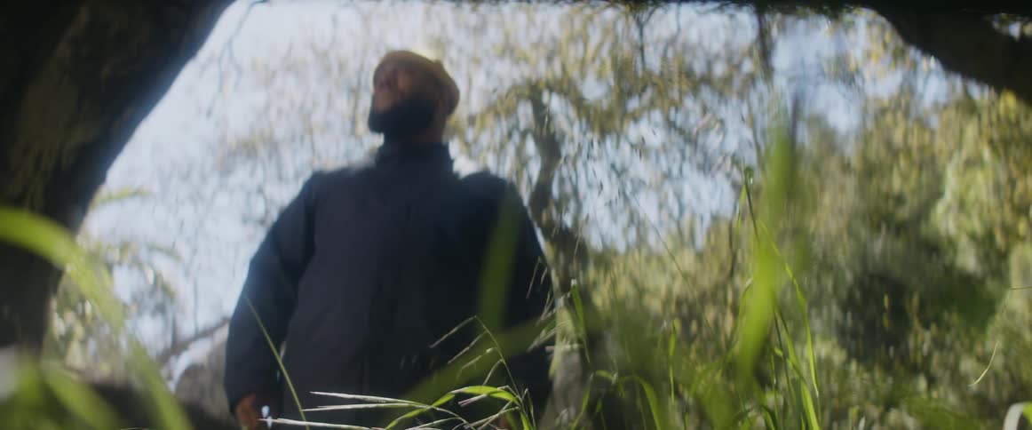 Man with beard yellow beanie and blue shirt stands in the forest