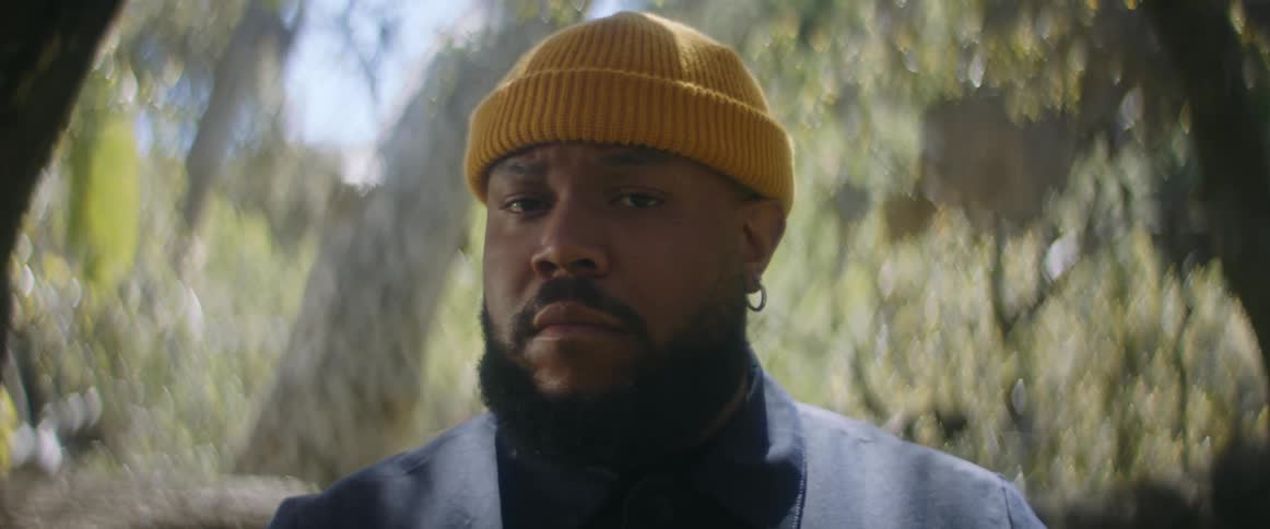 Man with yellow beanie beard and earrings looks around and at camera in the forest