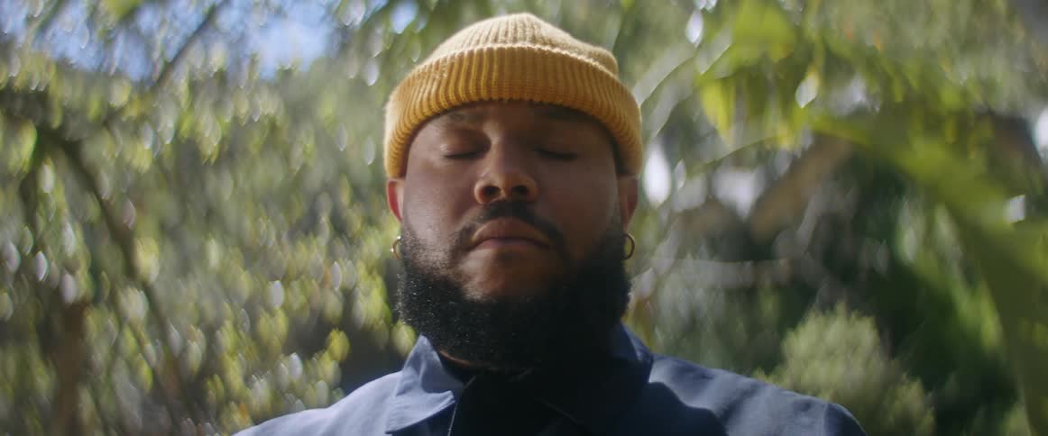 A man meditates with his eyes closed surrounded by vegetation