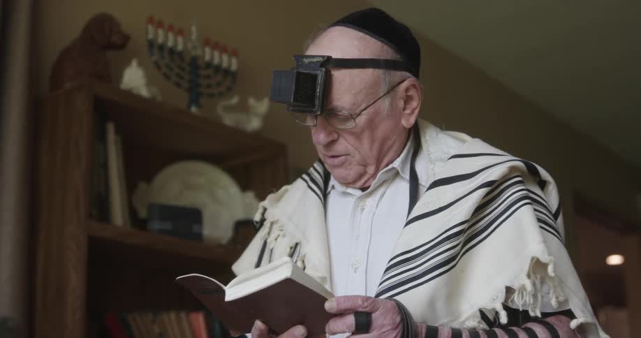 An elderly man participates in religious ritual while reading from a book